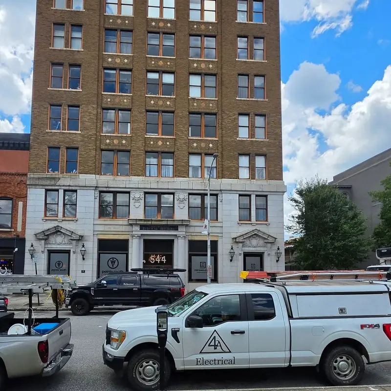 Two 4A Electrical trucks with ladder racks parked outside a historic downtown Macon building